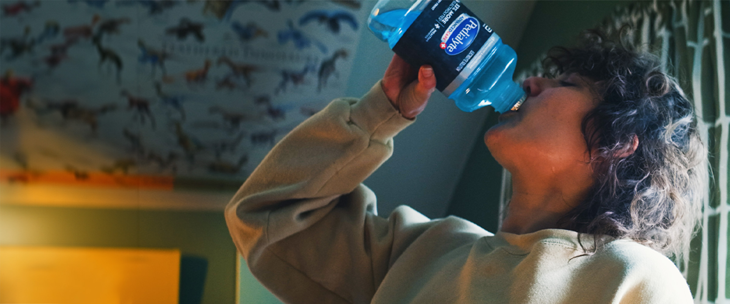 Adult woman drinking blue Pedialyte to hydrate while sick with a stomach bug.