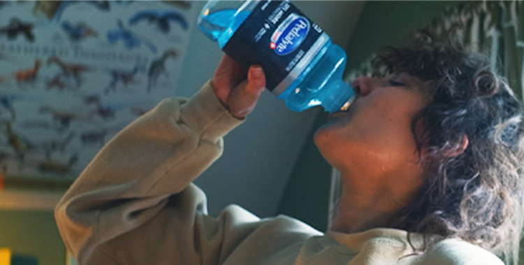 Adult woman drinking blue Pedialyte to hydrate while sick with a stomach bug.