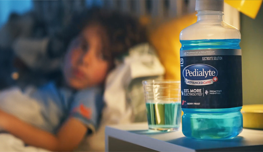Child in bed looking at blue Pedialyte liter with electrolytes to help hydrate during stomach flu symptoms.
